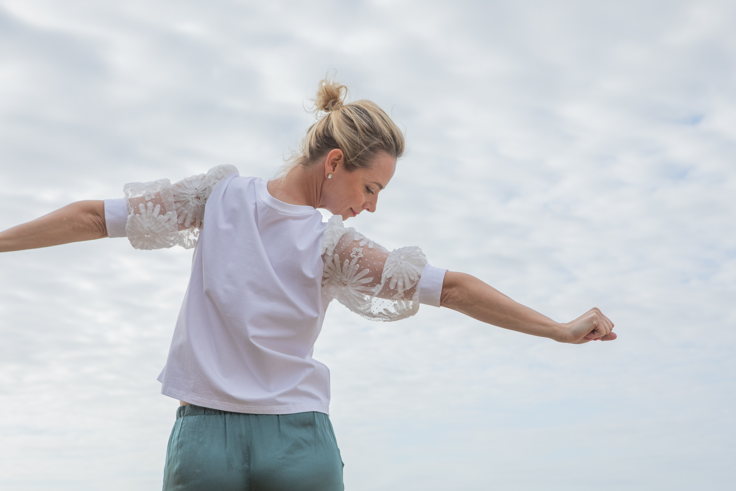 Jenny Heyer mit ausgebreiteten Armen vor bewölktem Himmel.