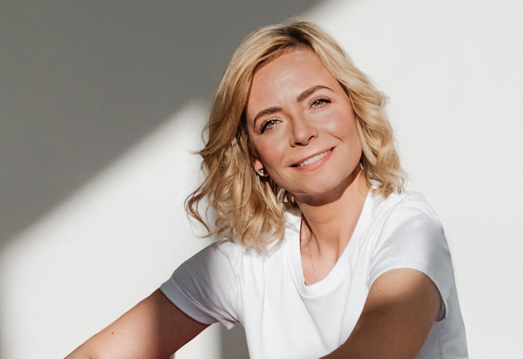 Porträt von Jenny Heyer im weißen T-Shirt vor heller Wand mit schrägem Schatten.