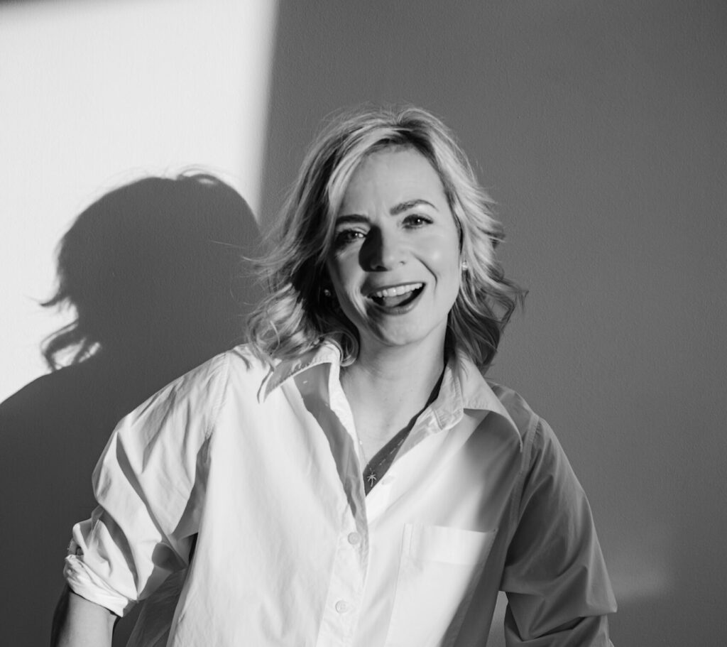 Schwarzweiß-Porträt von Jenny Heyer in weißer Bluse vor heller Wand mit Schatten.