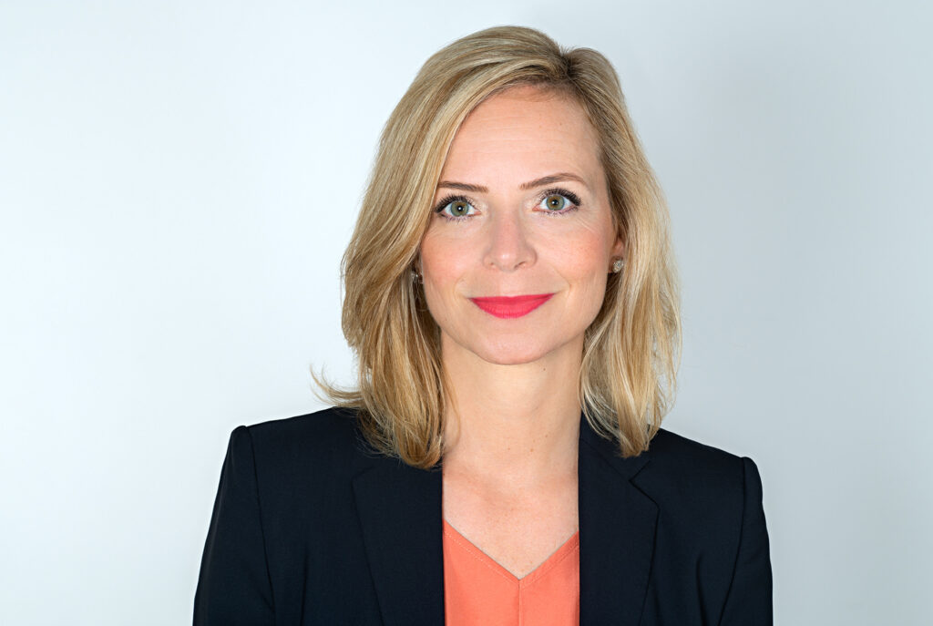 Porträt von Jenny Heyer im dunklen Blazer vor hellgrauem Hintergrund.