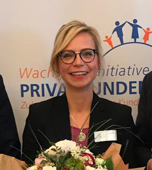 Jenny Heyer mit Brille und Blumenstrauß vor Veranstaltungswand zur Privatkunden-Initiative.